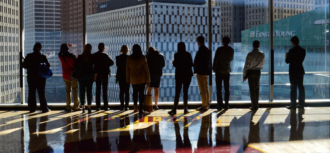 Business students silhouettes in front of a large window, with skyscrapers in the background