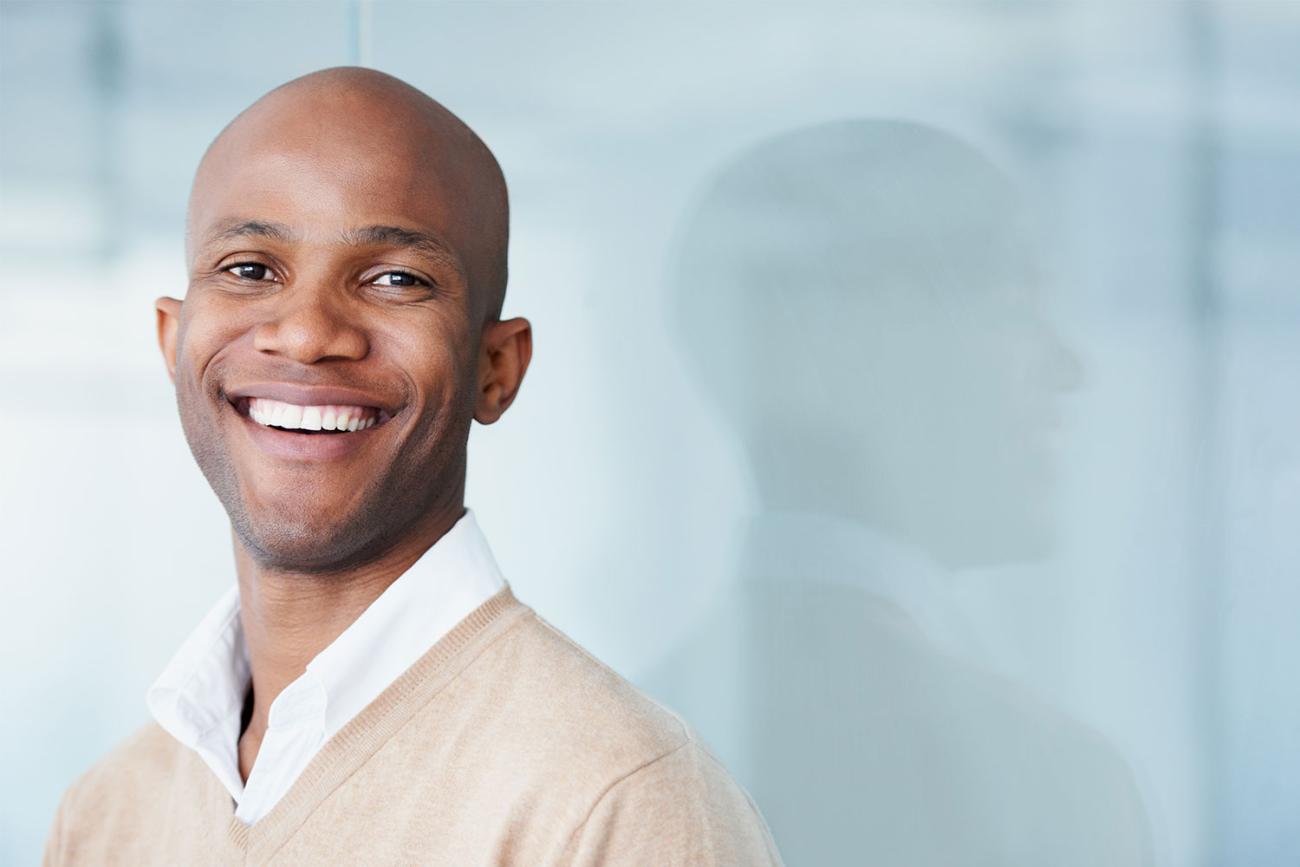 Smiling bald African American man in cream sweater standing in front of window