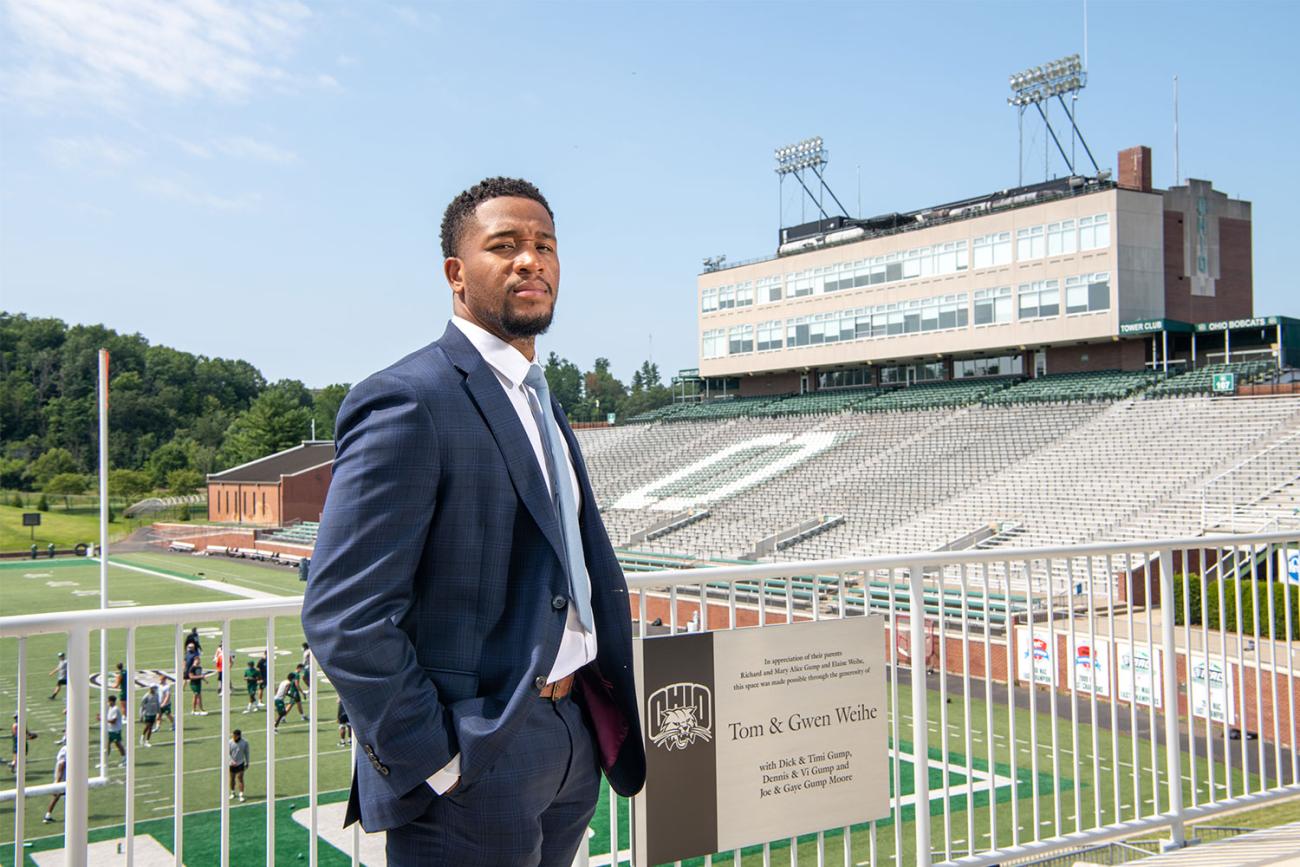 African American man in blue suit standing at railing overlooking football field