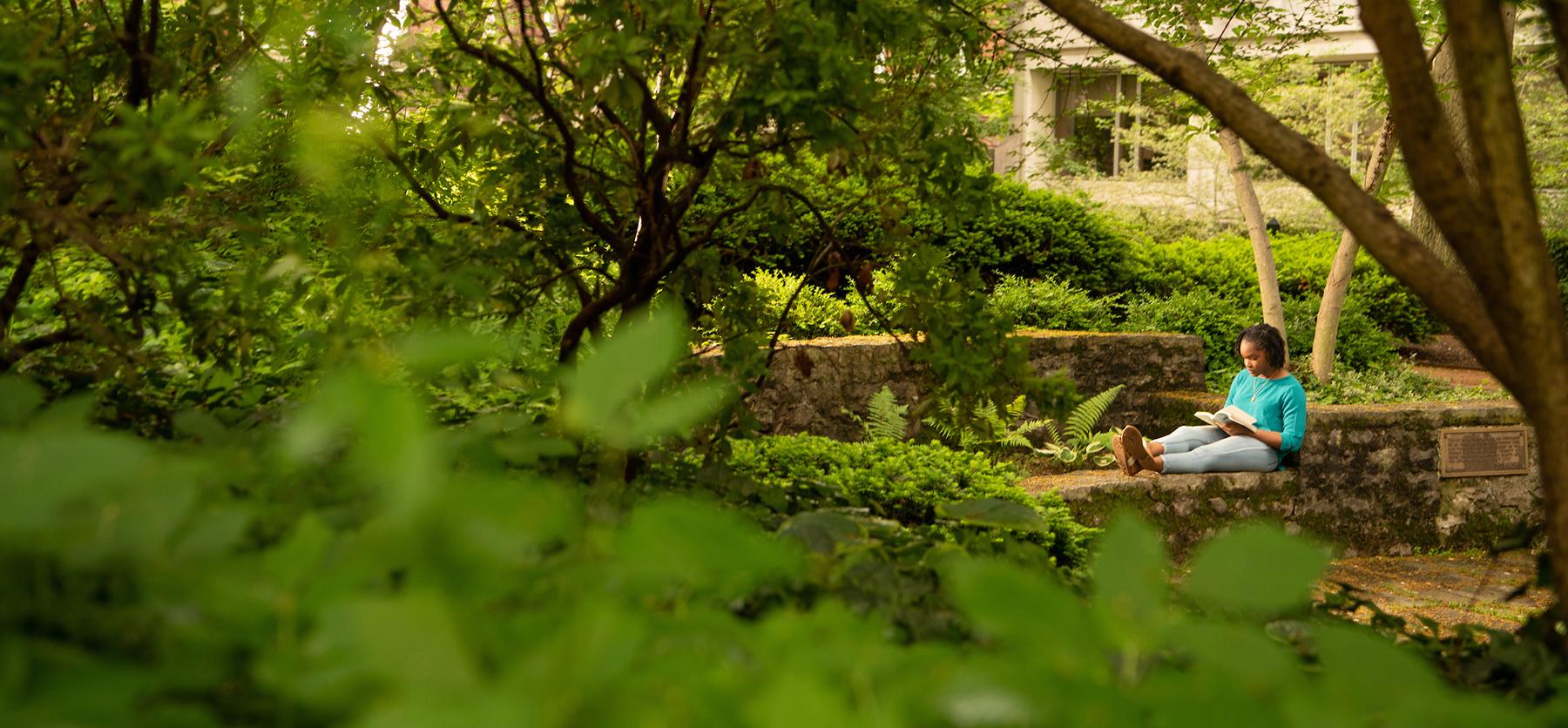 A student reads a book outside in the Wolfe Garden on the Athens Campus