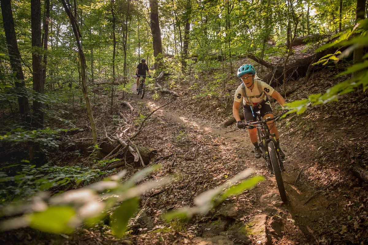 Two people ride mountain bikes on a wooded trail in Athens, Ohio