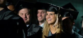 Student smiles while wearing her cap and gown at Commencement