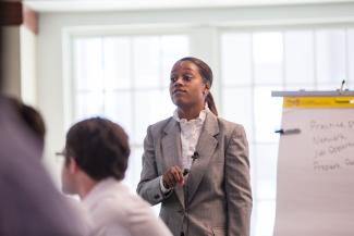 African American woman in gray suit with white shirt standing in front of white board