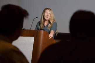 Blonde woman in dark green shirt smiling and standing at podium