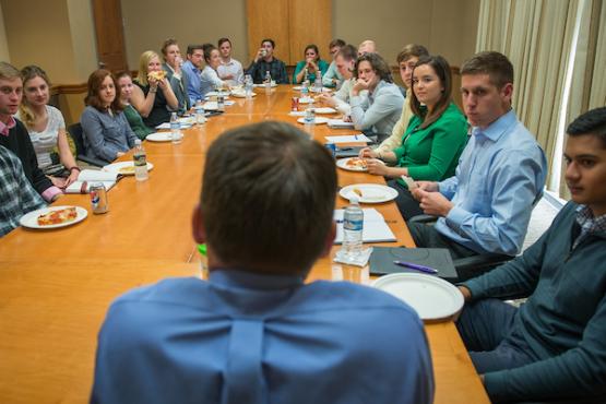 Business students listen to an alumnus speak all sitting around a conference table