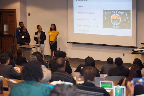 Business students present a powerpoint in a room full of attendees