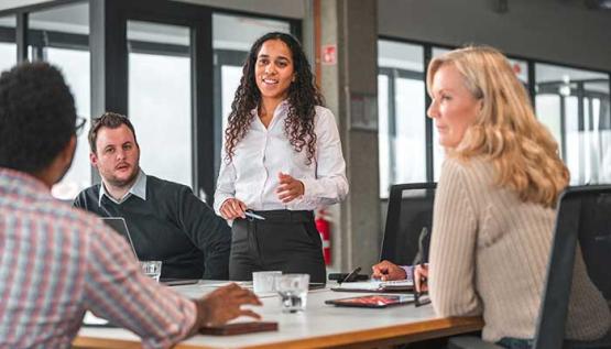 Female professional standing at a conference table and leading her team of peers in a discussion