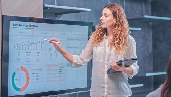 Professor of business analytics standing in front of screen showing students data analytics charts