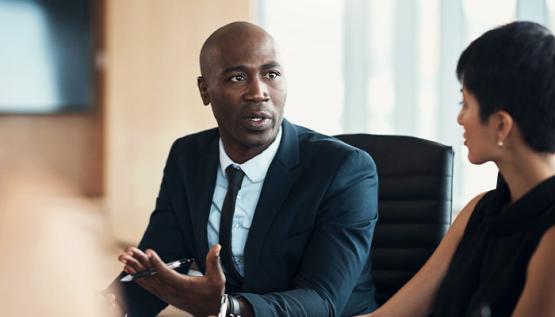 Male executive leader speaking with a colleague in a modern office meeting room, conveying leadership and professional collaboration.