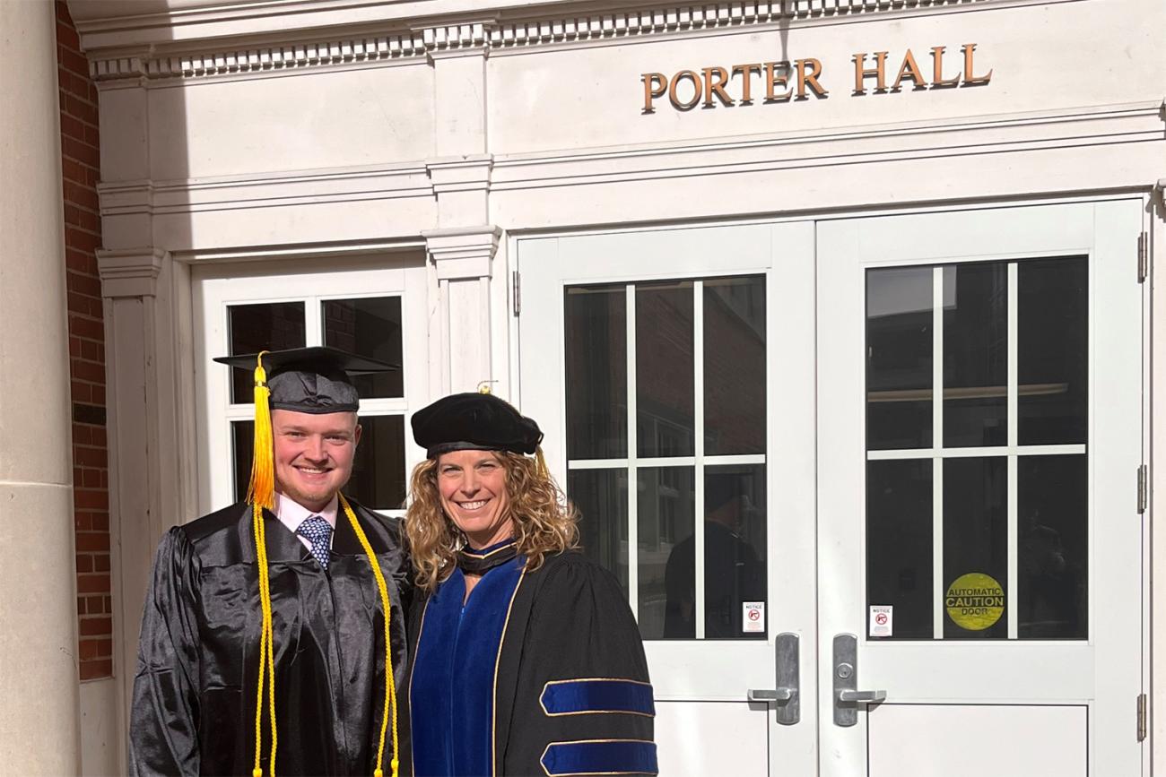 Julie Owens and graduate student in academic regalia in front of Porter Hall