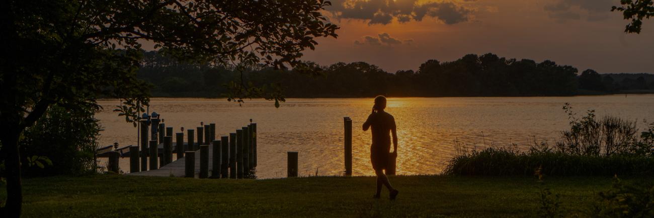 An OHIO student stands on the shore at sunset