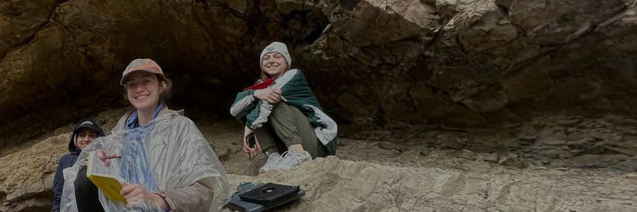 Geology students take a break on a ledge on the side of a mountain.
