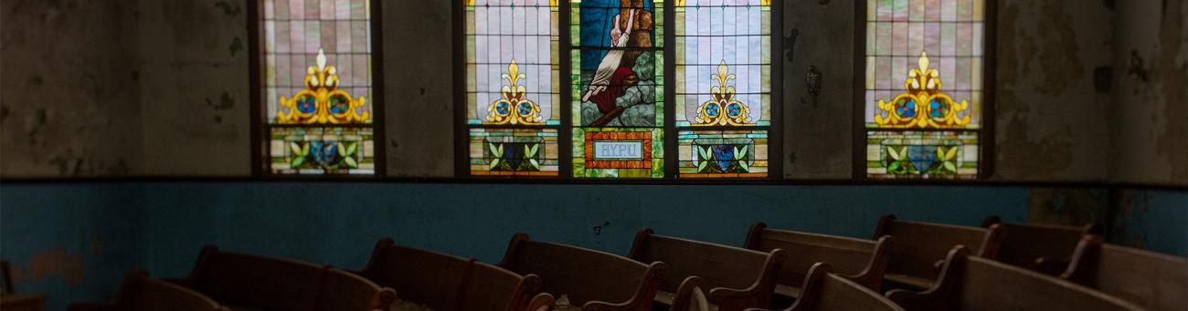 A view of a church with pews in front of a stained glass window.