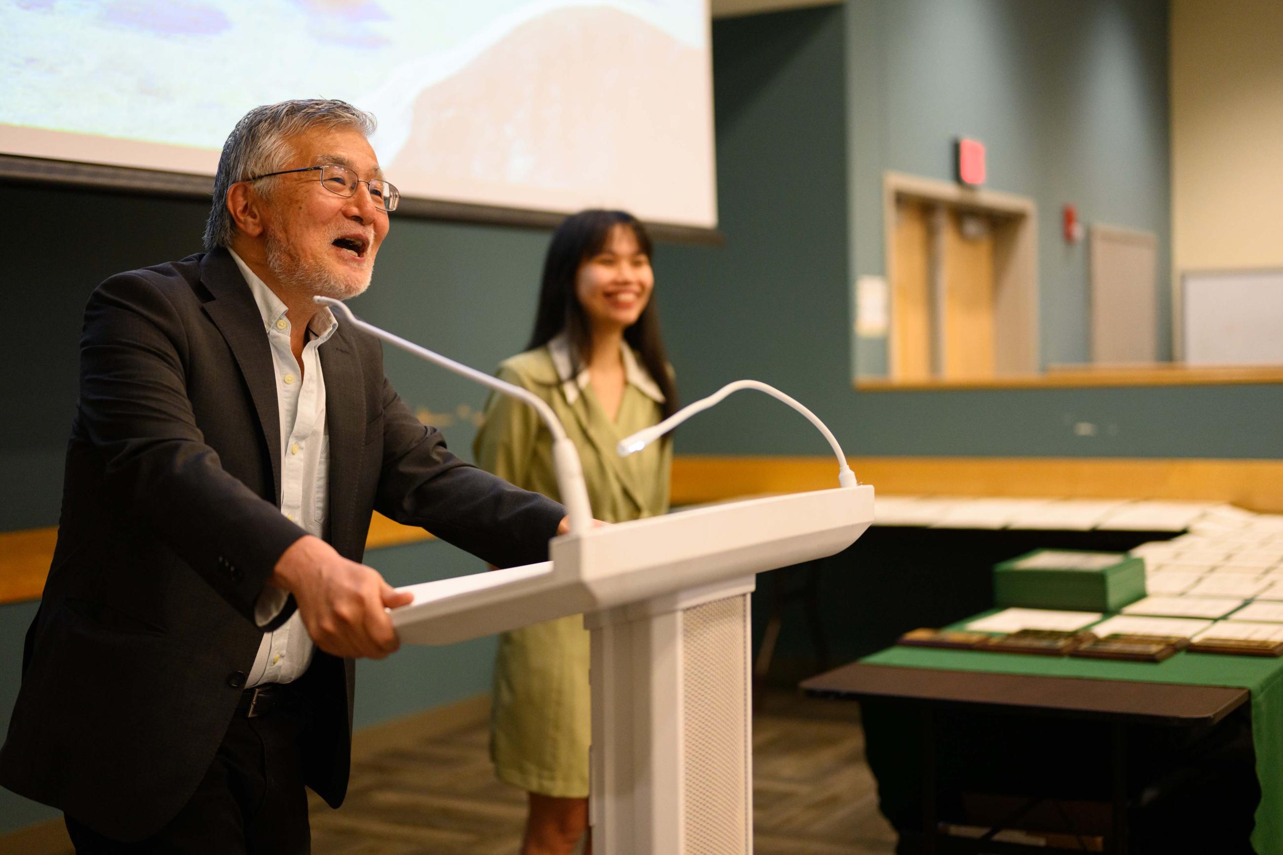 Dr. Suzuki at podium recognizing female student standing beside him.