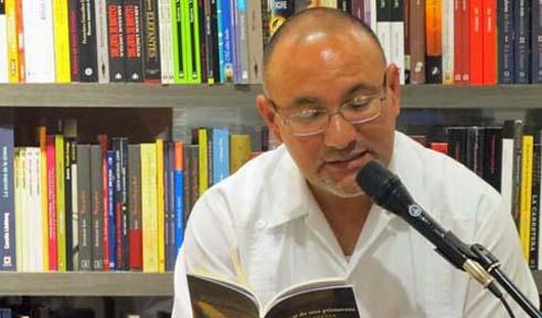 Daniel Torres, reading a book at microphone with bookshelves in background