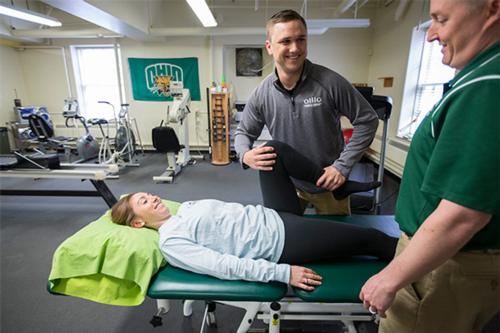 A man works with a patient, bending their knee in a physical therapy clinic