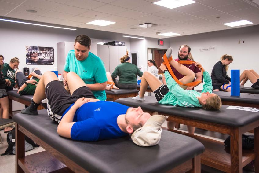Athletic training students stretch their classmates' legs on exam tables
