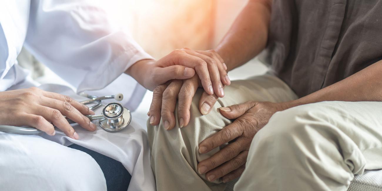 Closeup of a doctor holding hands with an elderly person
