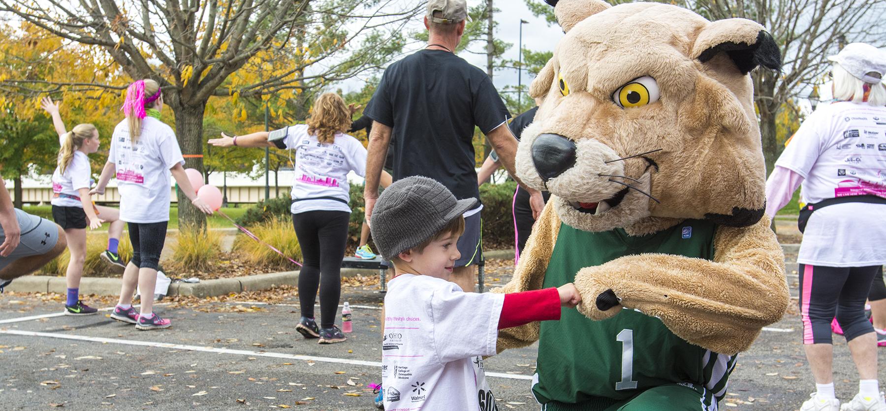 Rufus Bobcat giving a kid a fist bump at Race for the Cure