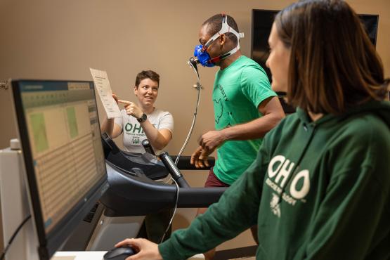 A person runs on a treadmill while two exercise physiologists perform a test.