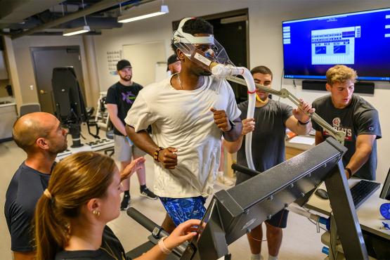 Exercise physiology students gather around to learn how to conduct a test with a person on a treadmill.