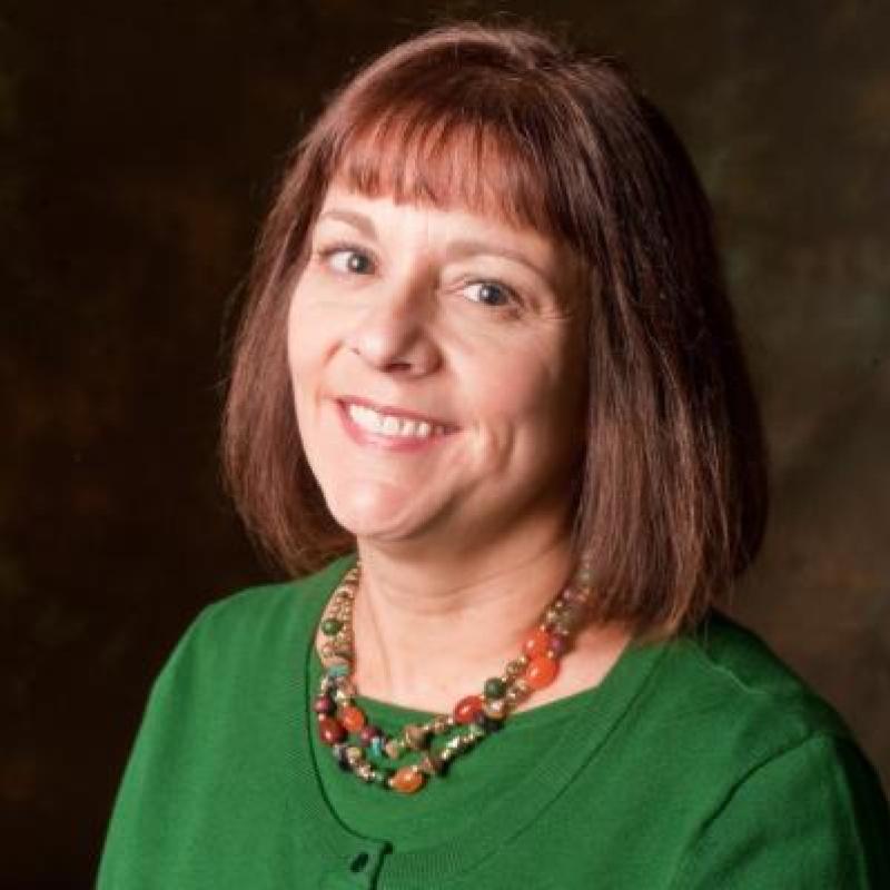 Valerie Miller smiling in a green cardigan in front of a neutral background.