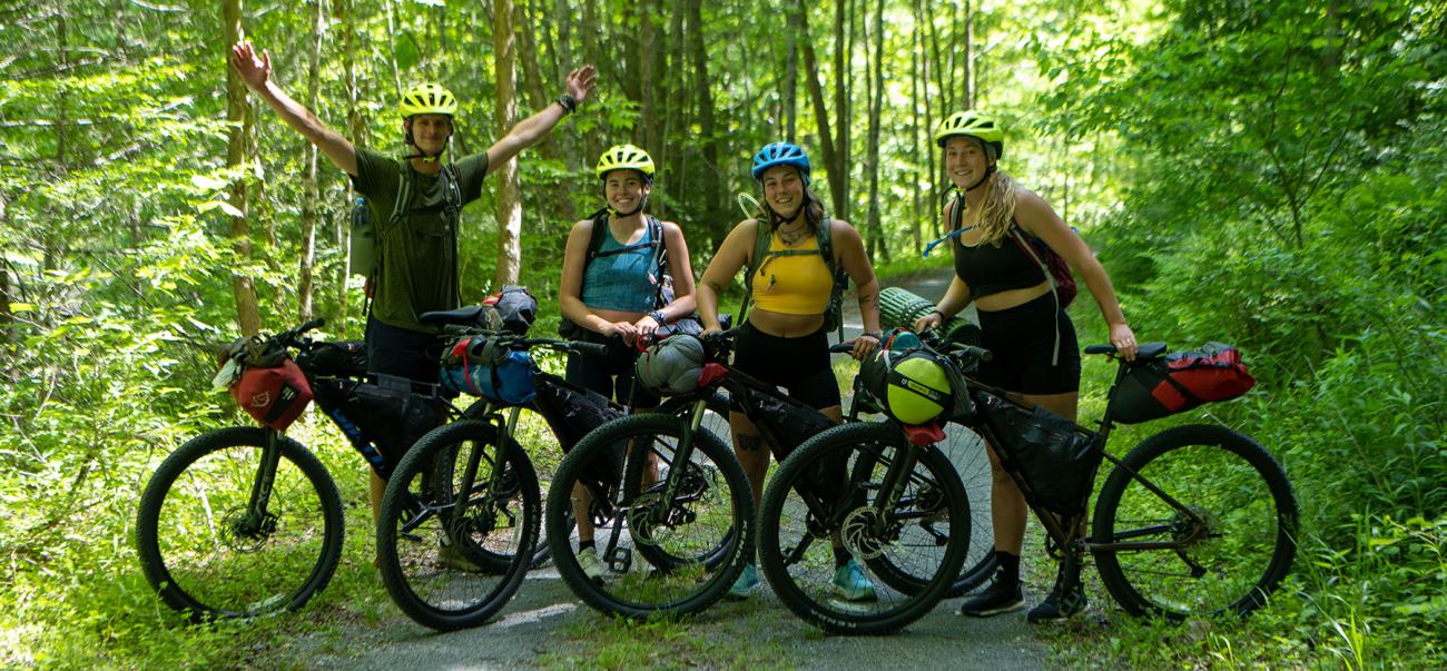Group of four students standing with their mountain bikes on a trail in the woods