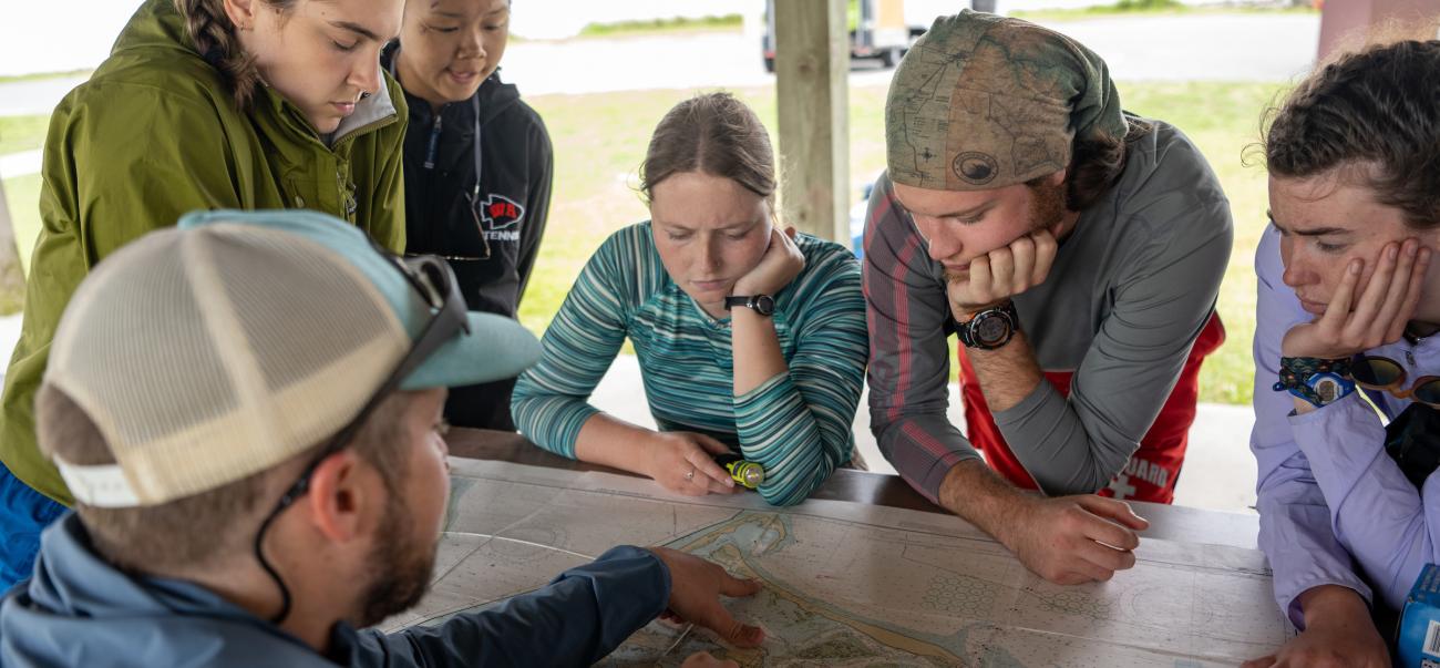 Students huddled around a map while an instructor points at a spot on the map