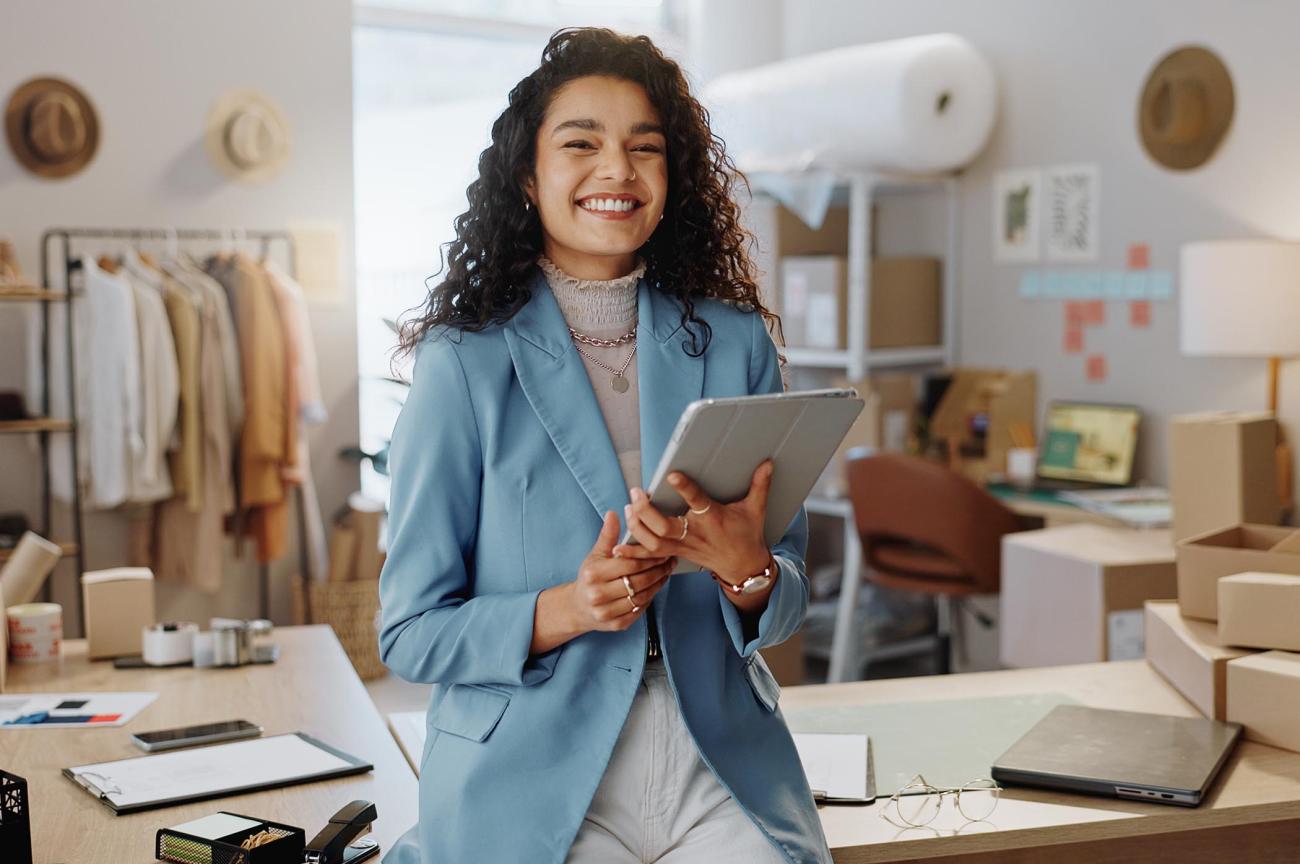 Smiling woman holding an ipad in an office surrounded by clothing and other displays.