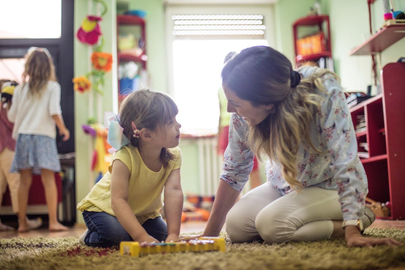 teacher looking at young child playing in classroom