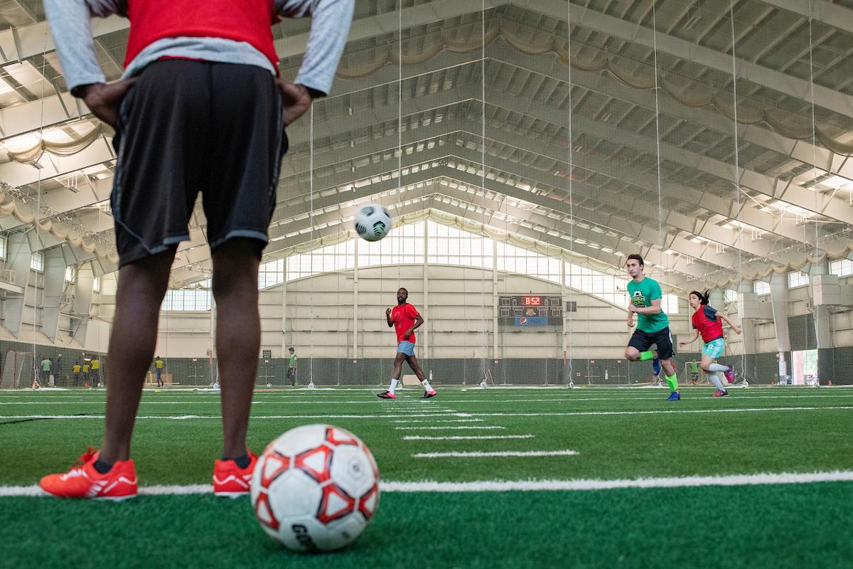 man stands on an indoor soccer pitch with a soccer ball in the foreground