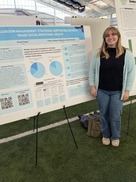 student standing next to their research poster at the student expo
