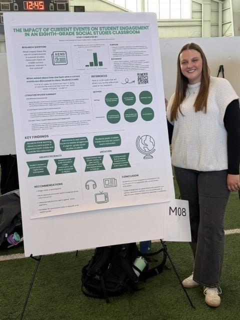 student standing next to their research poster at the student expo