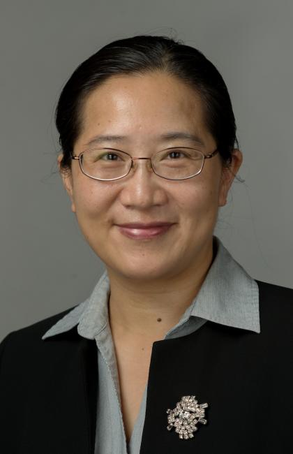 Headshot of a smiling Sandy Chen wearing glasses and a dark suit with a gray blouse