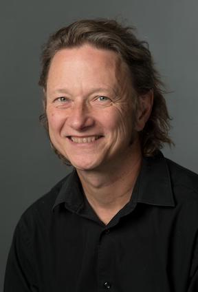 Headshot of a smiling Greg Kessler in a dark top