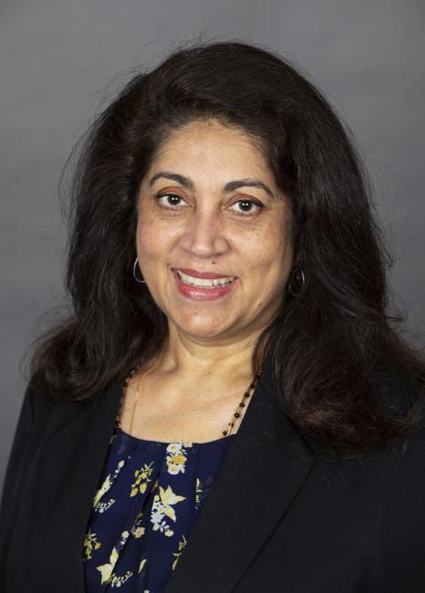 Headshot of a smiling Christine Bhat n a dark suit coat and print shirt