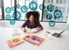 African American woman seated at a desk surrounded by research tools with interlocking gears overhead
