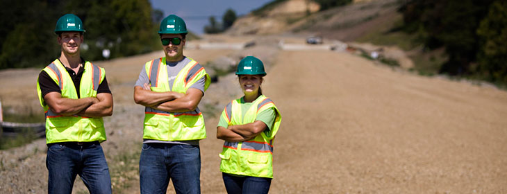 three construction workers standing in a work field in safety vests.