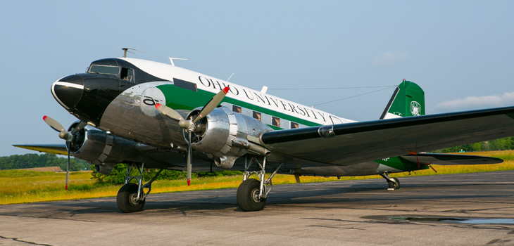 DC-3 painted green and white with "Ohio University" across the side, parked on landing strip