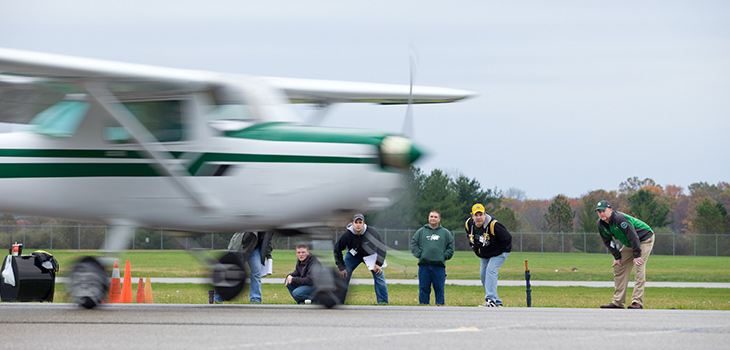 A group of people watch as a small plane lifts off a runway