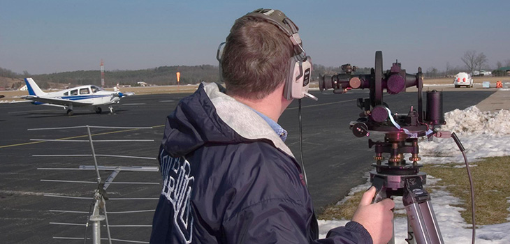 Person next to landing strip wearing headphones connected to a piece of equipment on a tripod