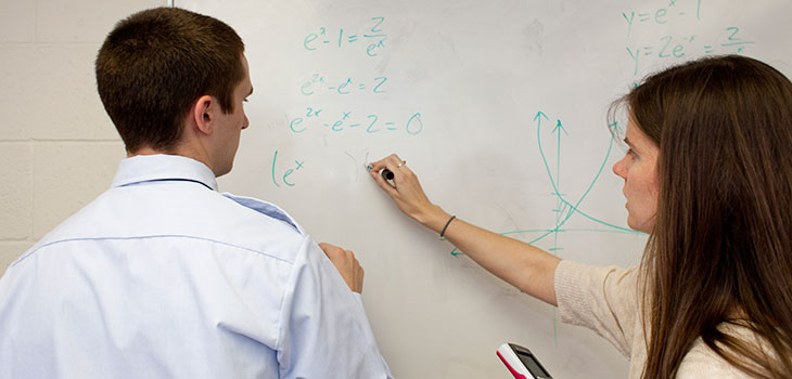 Man and woman writing math problems on whiteboard