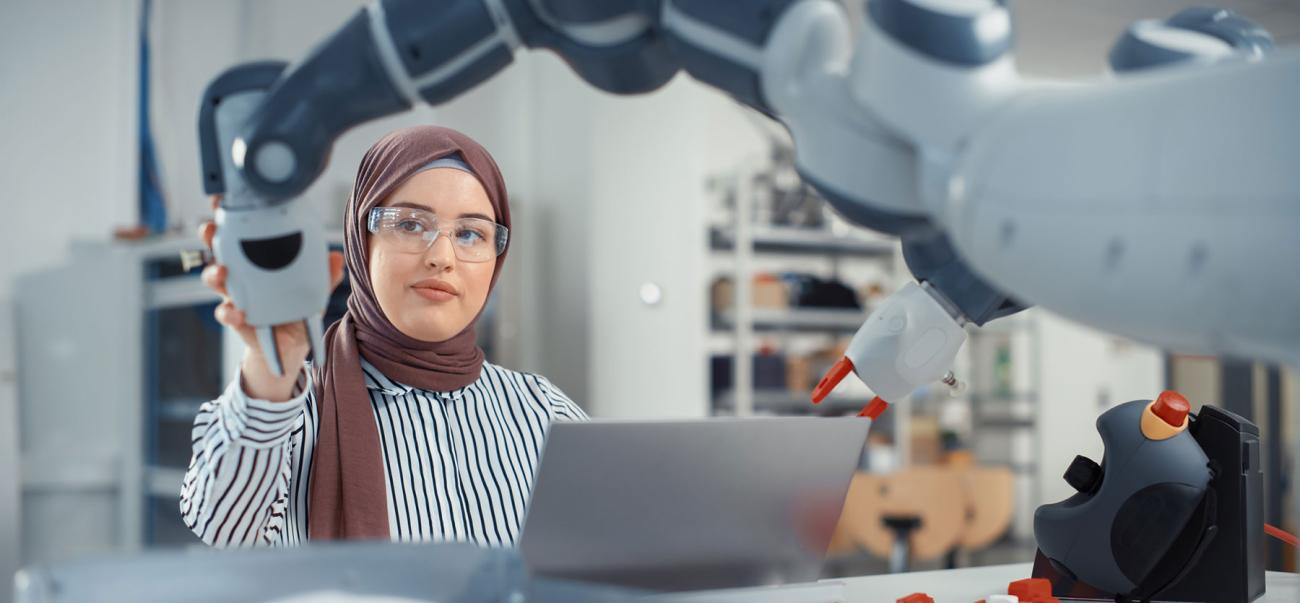 Woman in hijab standing behind robotic arm in an electrical engineering classroom