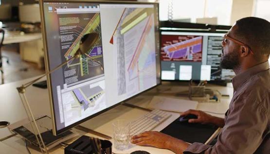 Civil engineer at desk with monitor showing construction plans