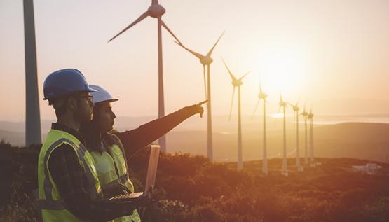 Two environmental engineers in safety vests standing outside next to wind turbines