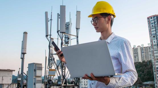 Engineer outside worksite in hardhat and holding laptop