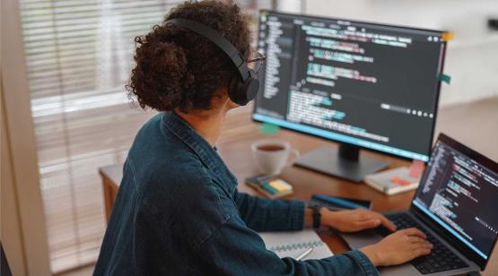 Computer engineer wearing headphones at desk reviewing code on monitor