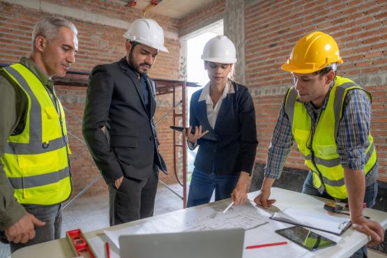 workers gathered around a table with papers on it.
