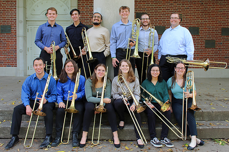 Students standing in front of brick architecture posing with trombones