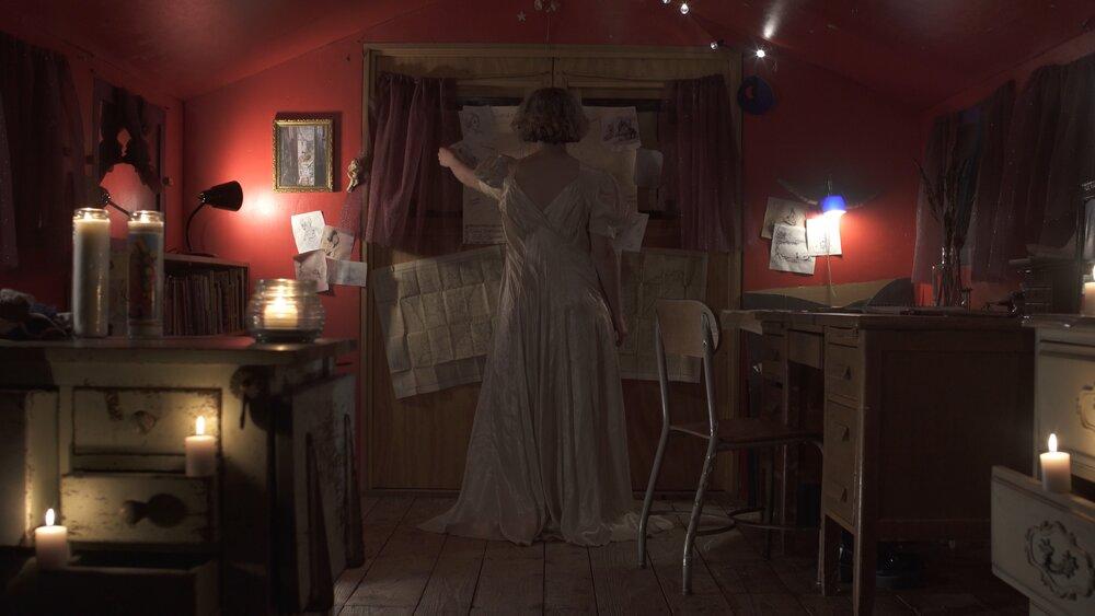 Julie Olivo acting in a decorated bedroom, wearing a pink dress.